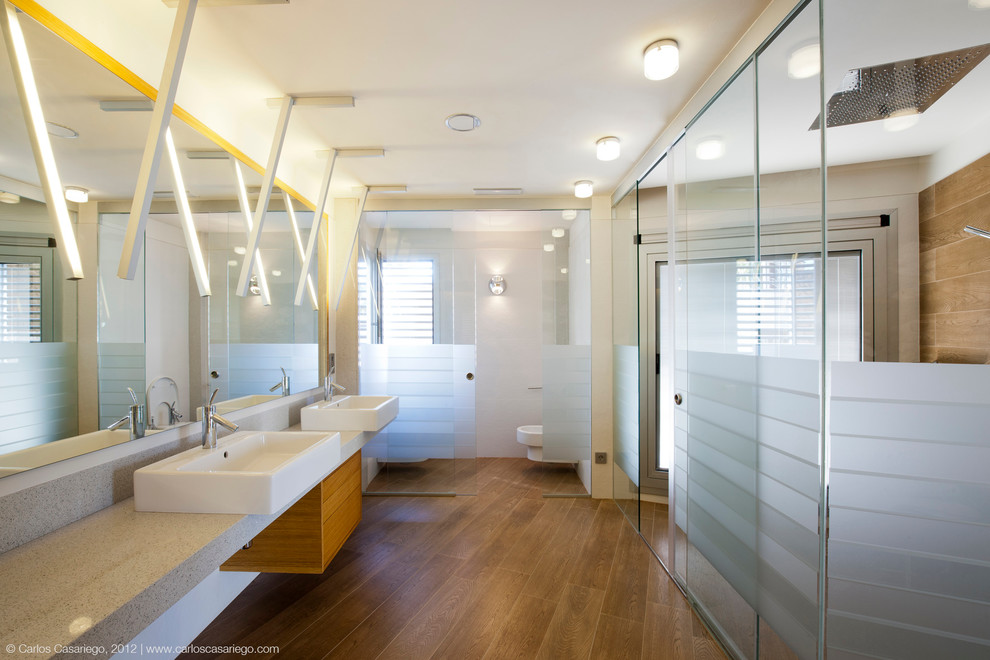 Cette image montre une très grande salle de bain principale design en bois brun avec un placard à porte plane, une douche à l'italienne, WC suspendus, un mur blanc, un sol en bois brun, une vasque et un plan de toilette en granite.