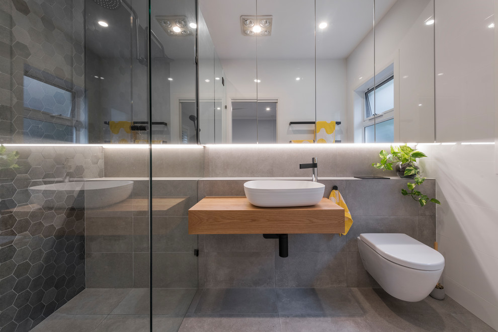 Diseño de cuarto de baño escandinavo con ducha empotrada, sanitario de pared, baldosas y/o azulejos grises, paredes grises, aseo y ducha, lavabo sobreencimera, encimera de madera, suelo gris y encimeras marrones