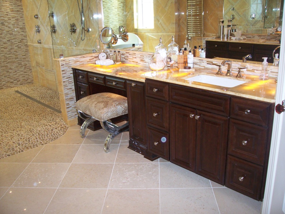 Aménagement d'une salle de bain classique en bois foncé avec un placard avec porte à panneau surélevé, un plan de toilette en onyx, un carrelage beige et un carrelage de pierre.