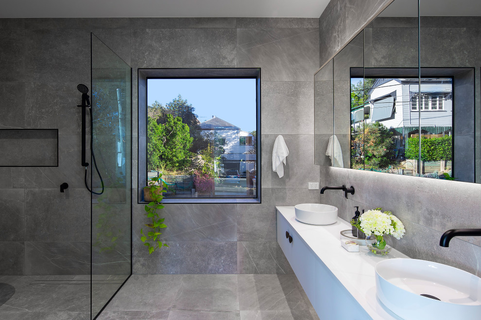 Modern inredning av ett vit vitt badrum, med grå kakel, stenkakel, grå väggar, betonggolv, grått golv, släta luckor, vita skåp, en kantlös dusch och ett fristående handfat