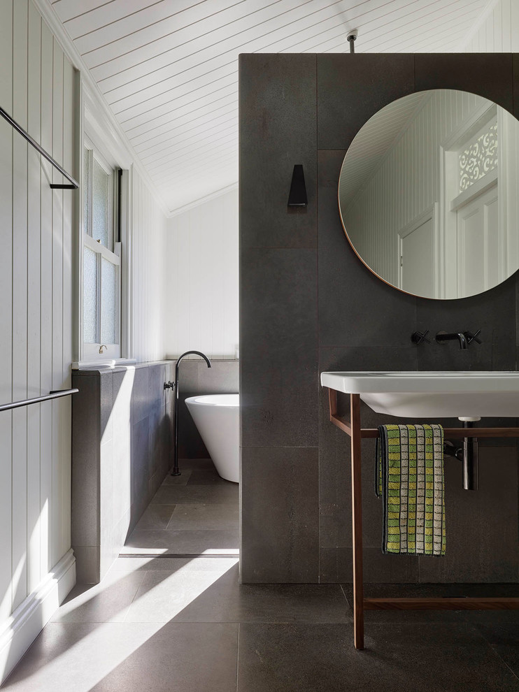 Cette image montre une salle de bain principale design avec une baignoire indépendante, un carrelage gris, un carrelage de pierre, un mur blanc et un lavabo suspendu.