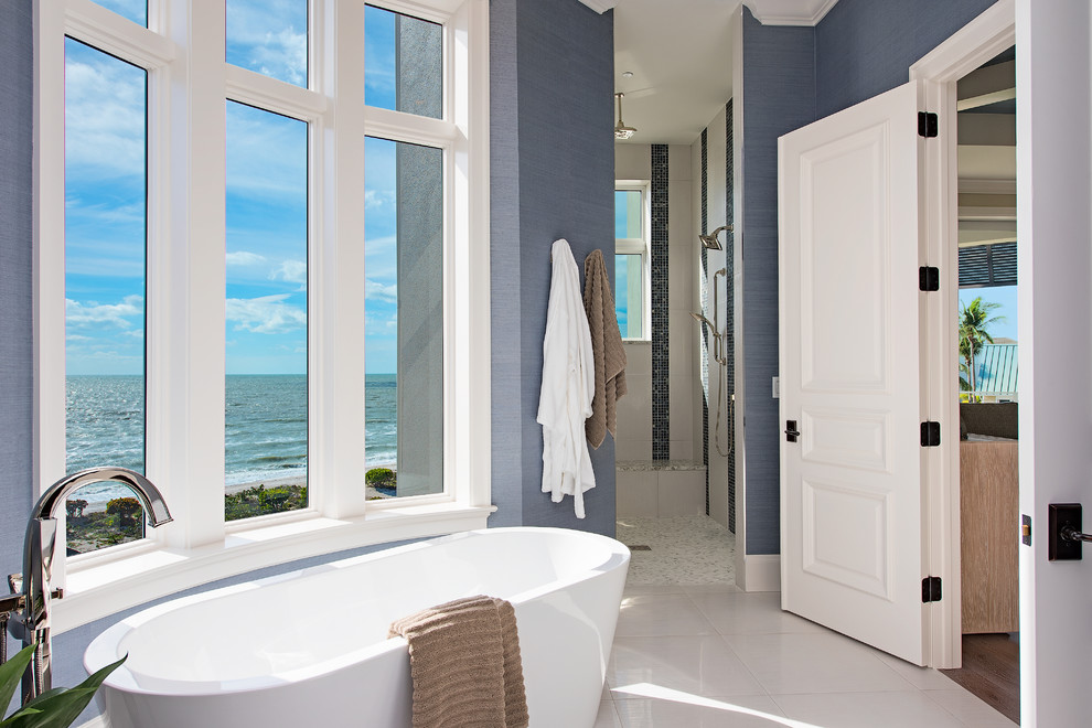 Exemple d'une salle de bain bord de mer avec une baignoire indépendante, un mur bleu et un sol blanc.