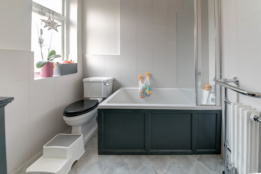 Medium sized traditional family bathroom in London with shaker cabinets, grey cabinets, a built-in bath, a shower/bath combination, a two-piece toilet, grey tiles, ceramic tiles, grey walls, ceramic flooring, a built-in sink, marble worktops, grey floors, a hinged door and black worktops.