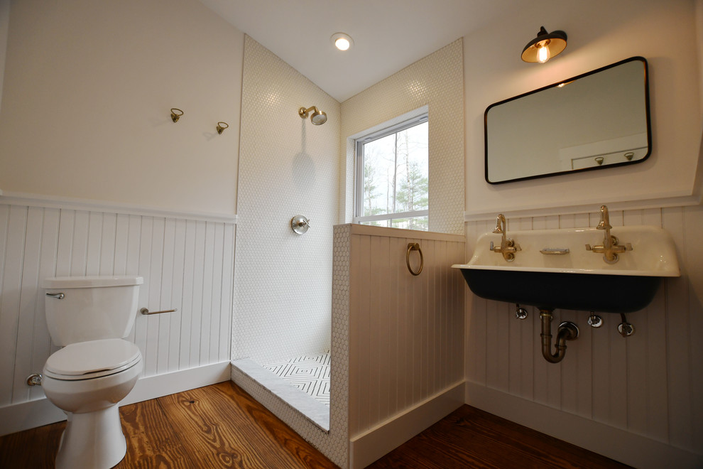 Foto på ett mellanstort lantligt badrum, med en dusch i en alkov, en toalettstol med separat cisternkåpa, vit kakel, keramikplattor, vita väggar, mellanmörkt trägolv, ett väggmonterat handfat, brunt golv och dusch med gångjärnsdörr