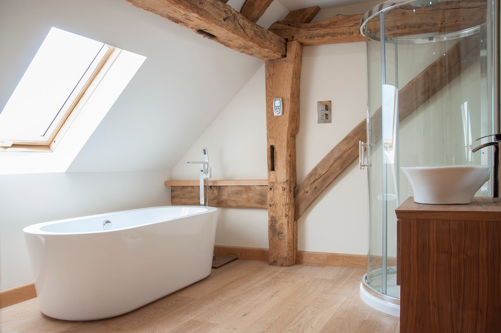 Modernes Badezimmer mit Aufsatzwaschbecken, hellbraunen Holzschränken, Waschtisch aus Holz, freistehender Badewanne, Duschnische, weißer Wandfarbe und hellem Holzboden in Surrey