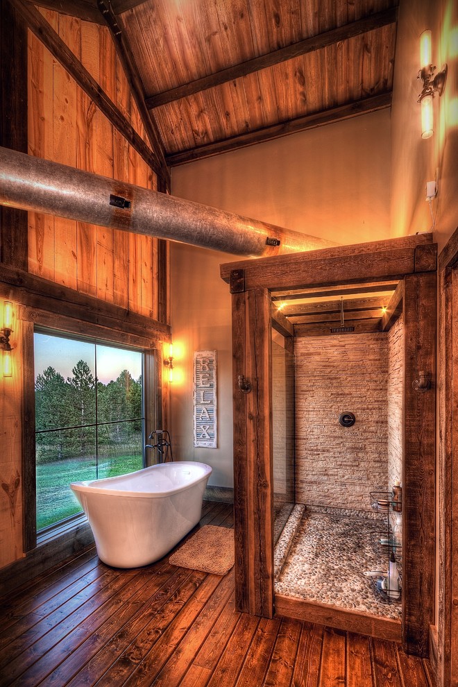 This is an example of a large rustic ensuite bathroom in Other with freestanding cabinets, white cabinets, a freestanding bath, a walk-in shower, a two-piece toilet, beige tiles, stone tiles, beige walls, medium hardwood flooring, a vessel sink, wooden worktops, brown floors, an open shower and beige worktops.