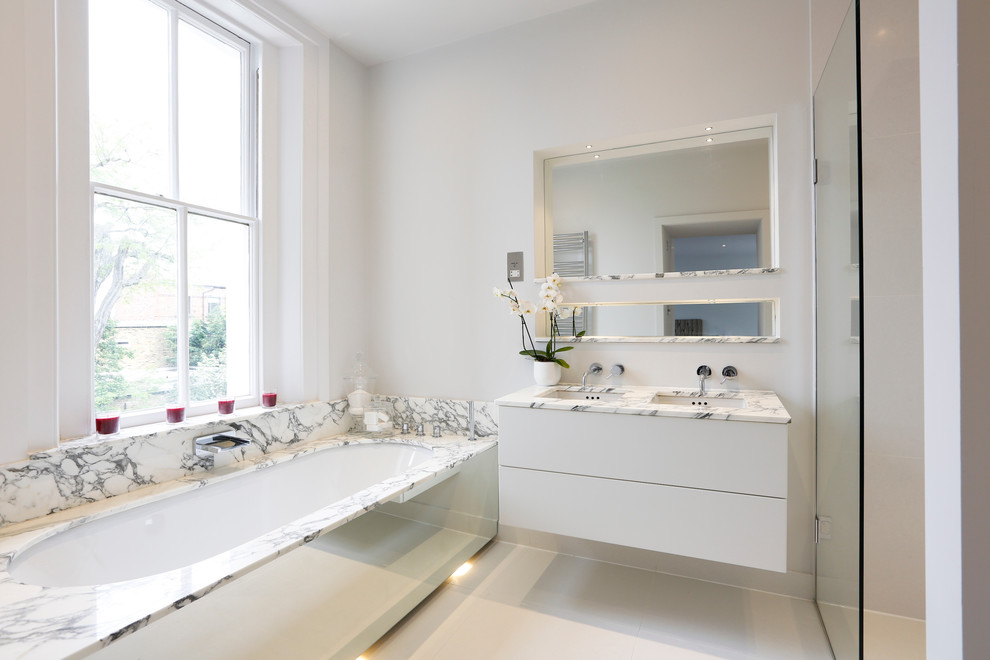 Пример оригинального дизайна: ванная комната в современном стиле с врезной раковиной, белыми фасадами и полновстраиваемой ванной
