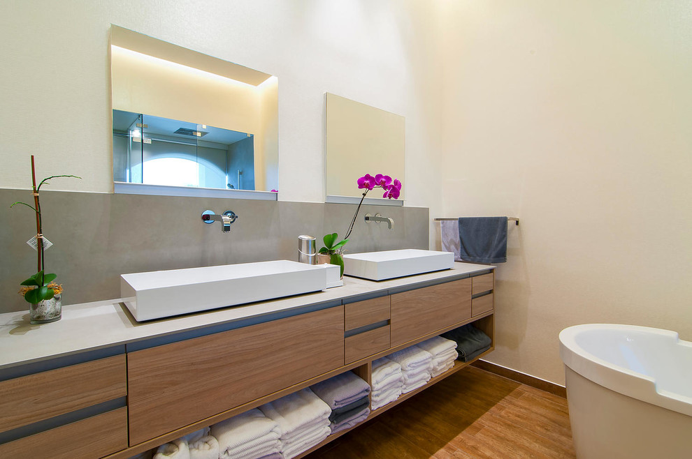 Idéer för att renovera ett stort funkis en-suite badrum, med ett fristående handfat, ett fristående badkar, en öppen dusch, en vägghängd toalettstol, släta luckor, skåp i mellenmörkt trä, grå kakel, vita väggar och mellanmörkt trägolv