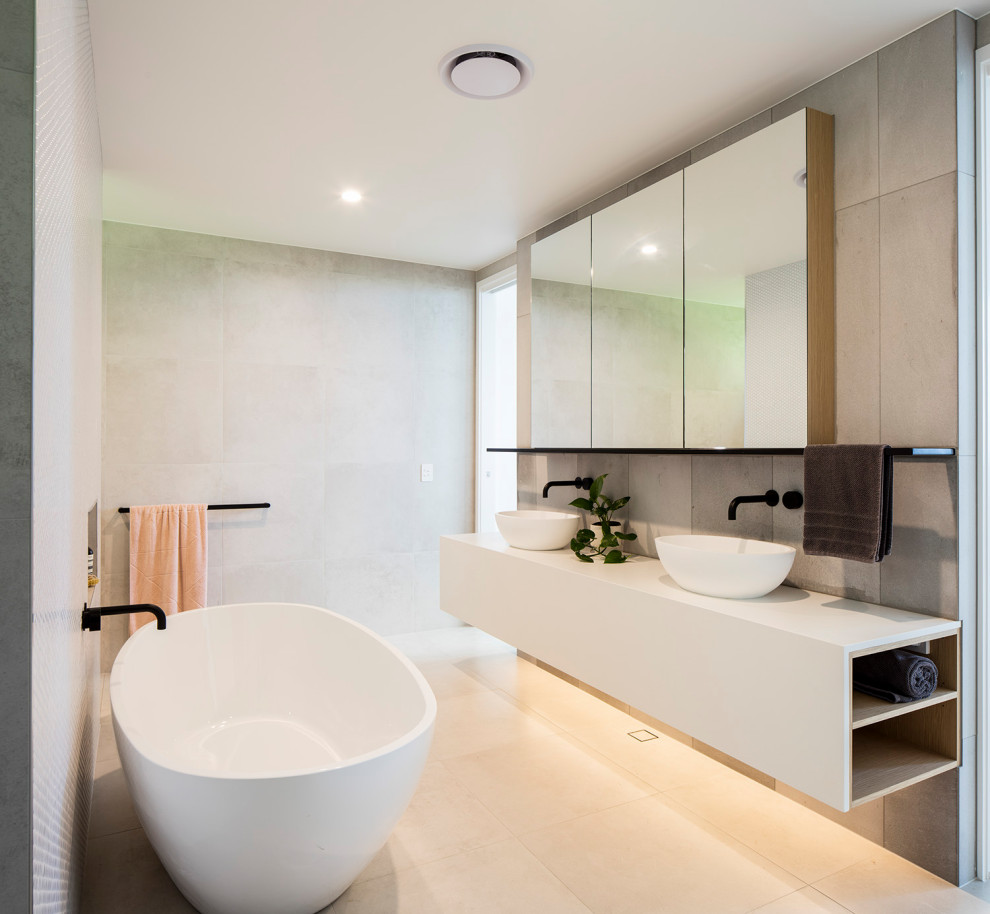 Modelo de cuarto de baño doble y flotante contemporáneo con bañera exenta, baldosas y/o azulejos grises, lavabo sobreencimera, suelo beige y encimeras blancas