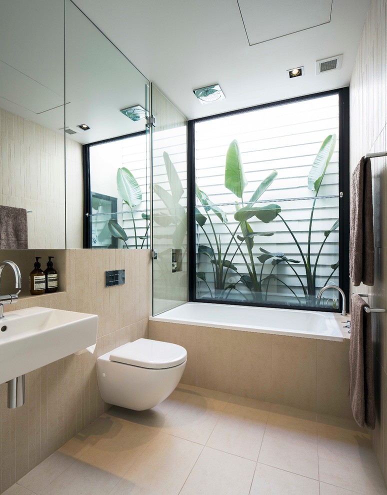 На фото: ванная комната среднего размера в стиле модернизм с подвесной раковиной, инсталляцией, бежевой плиткой и ванной в нише с
