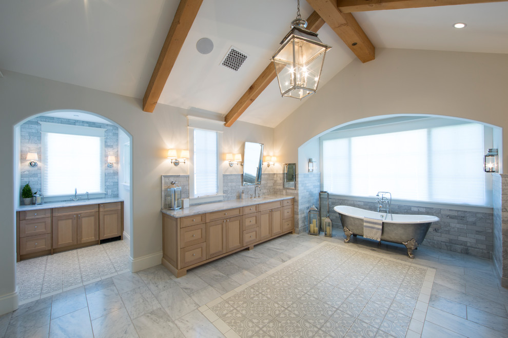Cette image montre une grande salle de bain principale traditionnelle en bois clair avec un placard à porte shaker, une baignoire sur pieds, un carrelage gris, un carrelage métro, un mur beige, un sol en carrelage de porcelaine, un lavabo encastré et un sol gris.
