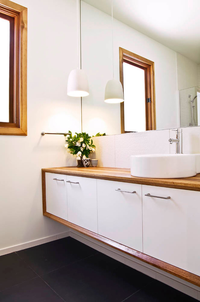 На фото: ванная комната в современном стиле с настольной раковиной, плоскими фасадами, белыми фасадами, столешницей из дерева, белой плиткой, керамической плиткой, белыми стенами, полом из керамической плитки и коричневой столешницей с