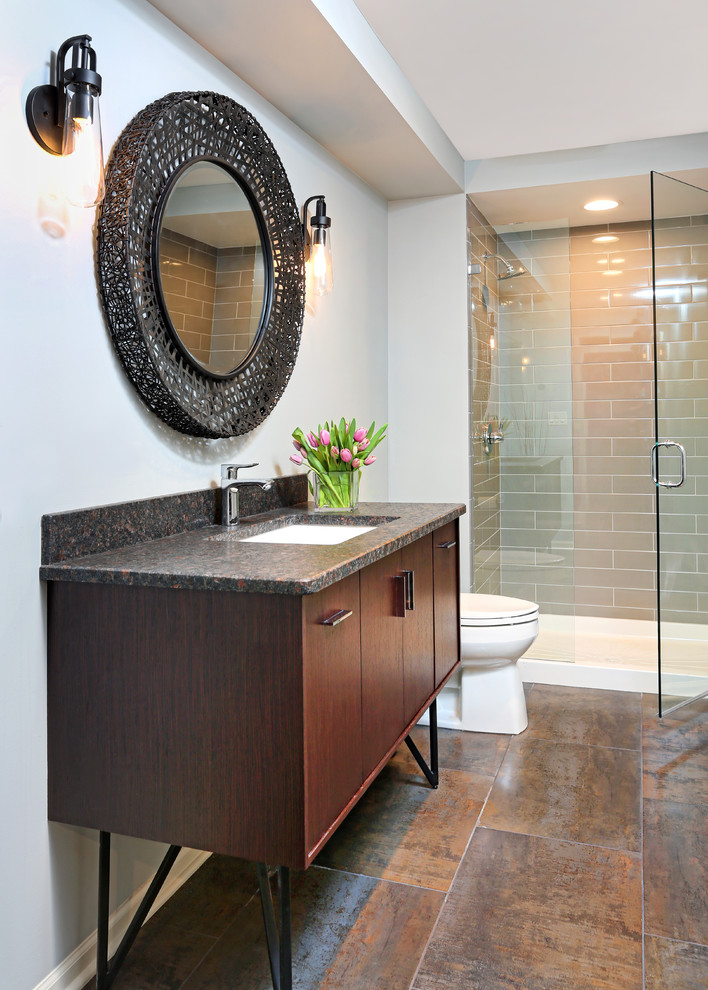 Eklektisk inredning av ett mellanstort badrum med dusch, med ett undermonterad handfat, släta luckor, skåp i mellenmörkt trä, granitbänkskiva, en dusch i en alkov, en toalettstol med hel cisternkåpa, brun kakel, porslinskakel, grå väggar och klinkergolv i porslin