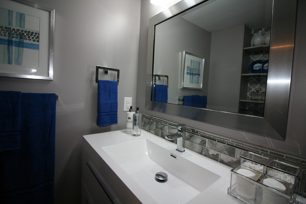 Photo of a medium sized contemporary family bathroom in Ottawa with flat-panel cabinets, white cabinets, an alcove bath, a two-piece toilet, grey tiles, glass sheet walls, grey walls, ceramic flooring, an integrated sink, solid surface worktops, white floors and white worktops.