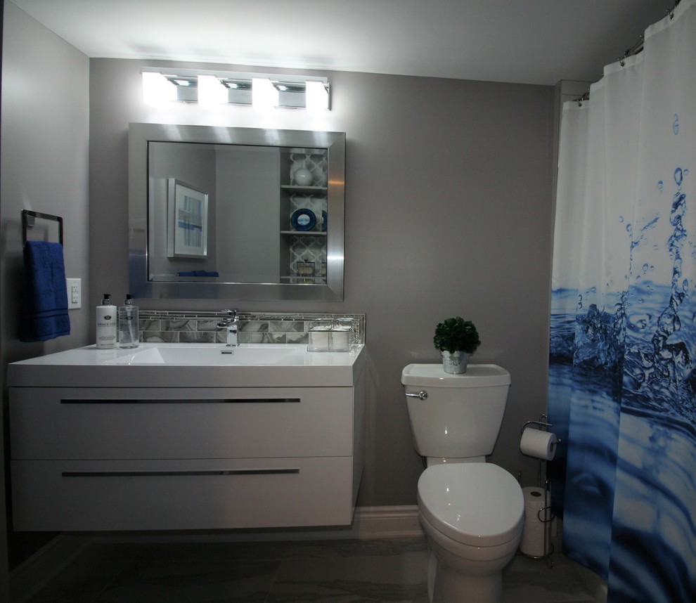 Inspiration for a medium sized contemporary family bathroom in Ottawa with flat-panel cabinets, white cabinets, an alcove bath, a two-piece toilet, grey tiles, glass sheet walls, grey walls, ceramic flooring, an integrated sink, solid surface worktops, white floors and white worktops.