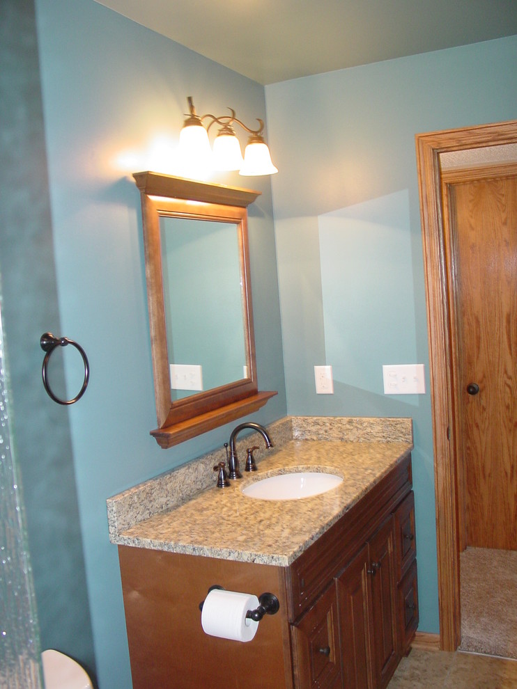 Bild på ett mellanstort vintage badrum med dusch, med ett undermonterad handfat, luckor med infälld panel, skåp i mellenmörkt trä, granitbänkskiva, en dusch i en alkov, en toalettstol med separat cisternkåpa, blå väggar och linoleumgolv