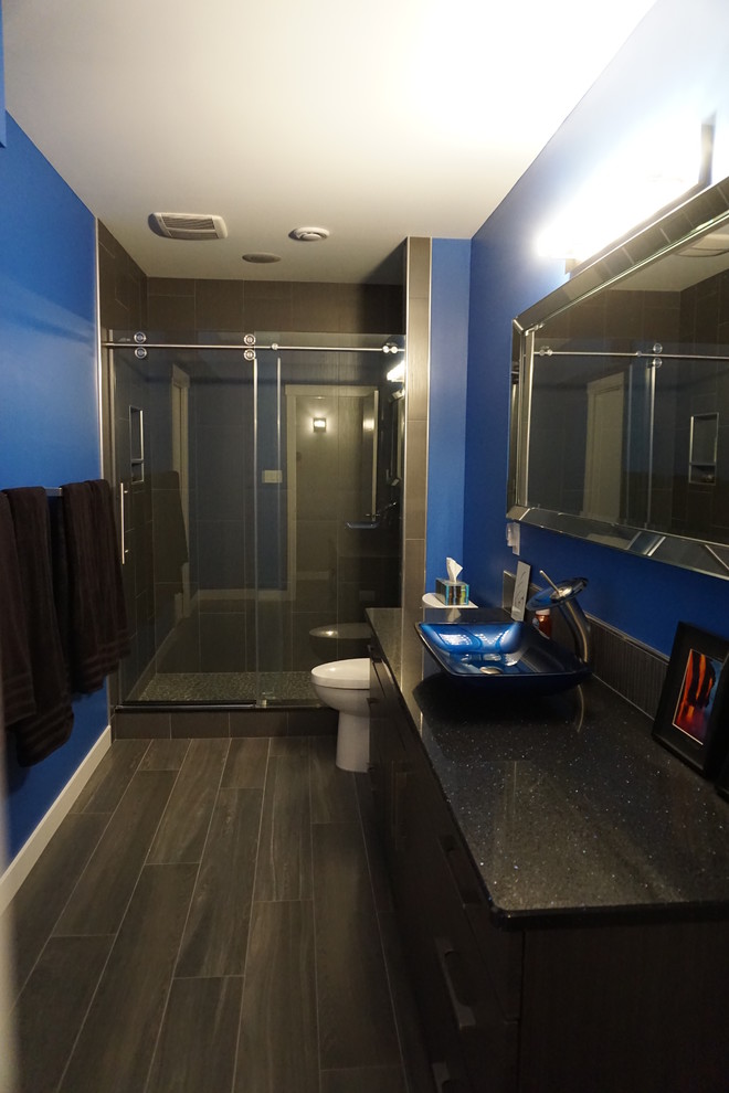 Réalisation d'une salle de bain minimaliste en bois foncé avec un mur bleu, une vasque, un placard à porte plane, un carrelage gris et un plan de toilette en granite.