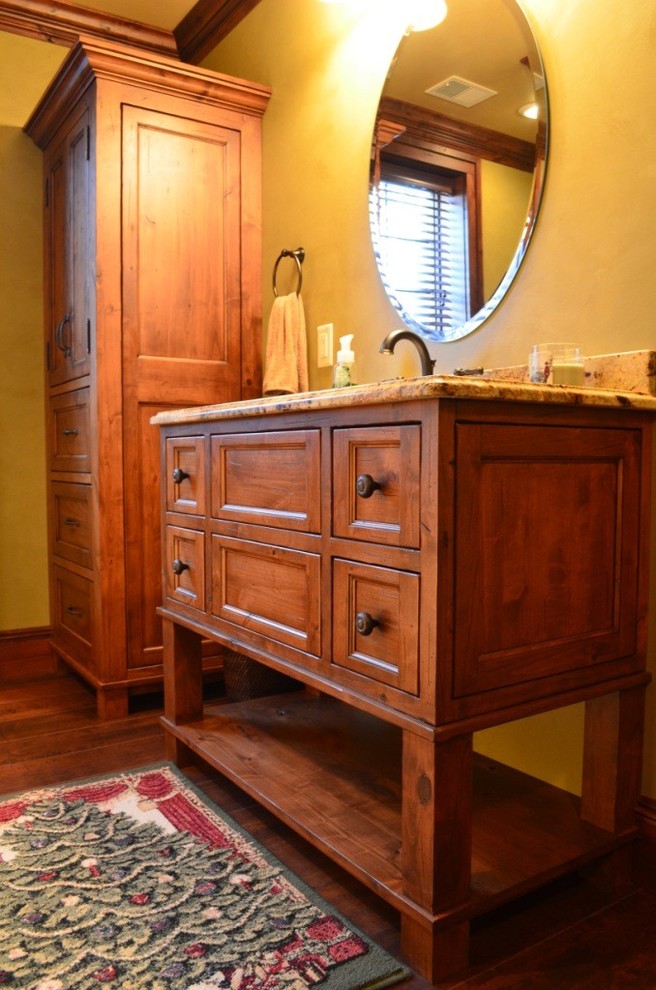 Réalisation d'une salle d'eau chalet en bois brun de taille moyenne avec un lavabo encastré, un placard en trompe-l'oeil, un plan de toilette en granite, un mur jaune et un sol en bois brun.