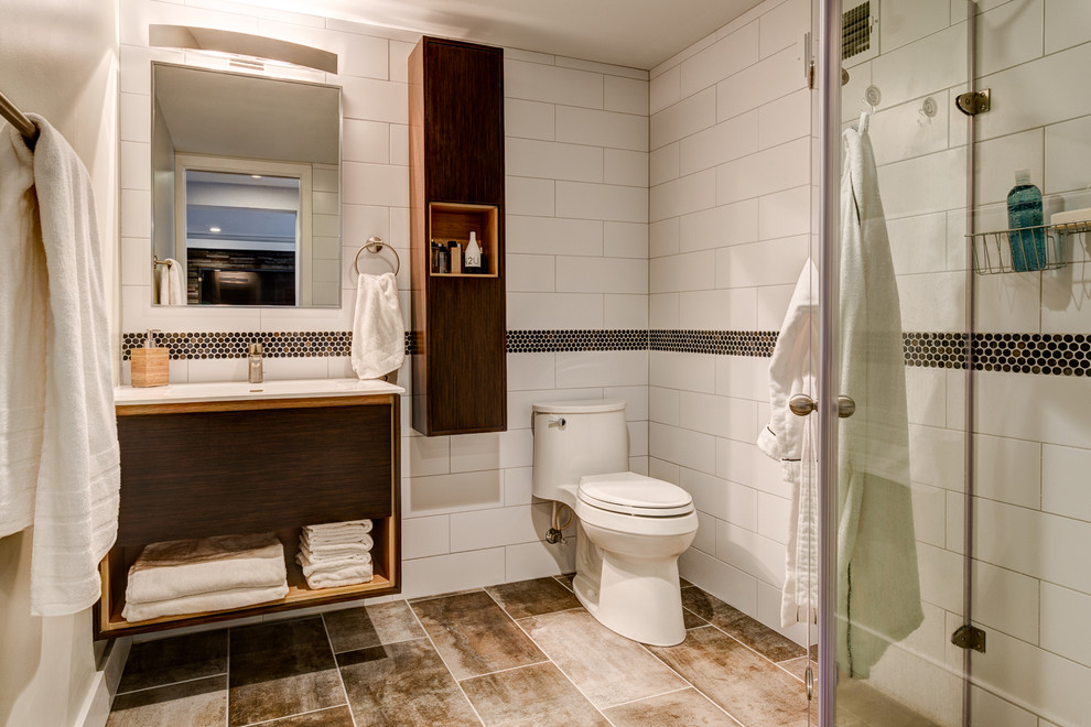 Bild på ett litet funkis badrum med dusch, med släta luckor, skåp i mellenmörkt trä, en toalettstol med hel cisternkåpa, vit kakel, keramikplattor, vita väggar, klinkergolv i keramik, ett integrerad handfat, bänkskiva i akrylsten och en hörndusch