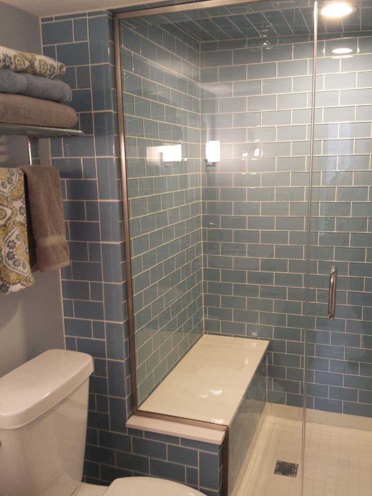 Modern inredning av ett litet bastu, med vita skåp, granitbänkskiva, en toalettstol med separat cisternkåpa, blå kakel, glaskakel, släta luckor, en dusch i en alkov, blå väggar, ett undermonterad handfat, klinkergolv i porslin och dusch med gångjärnsdörr