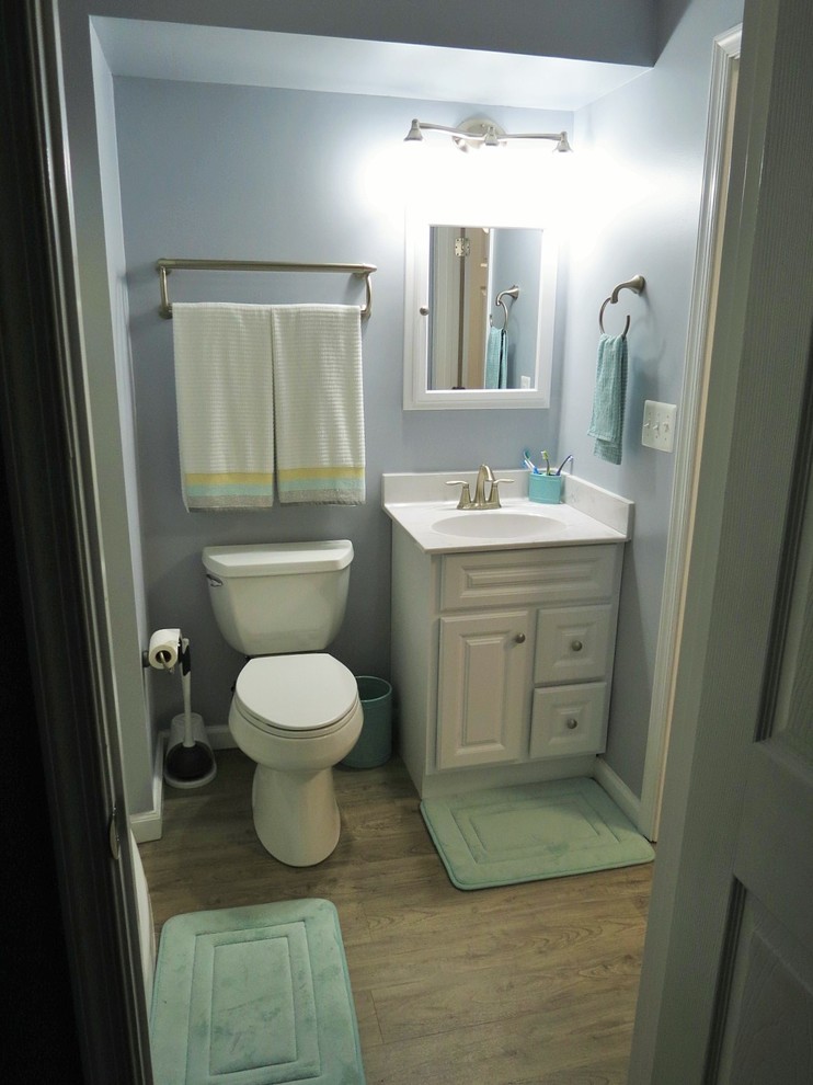 Cette image montre une petite salle de bain traditionnelle avec un placard avec porte à panneau surélevé, des portes de placard blanches, WC à poser, un mur gris, un sol en vinyl, un plan vasque et un plan de toilette en marbre.