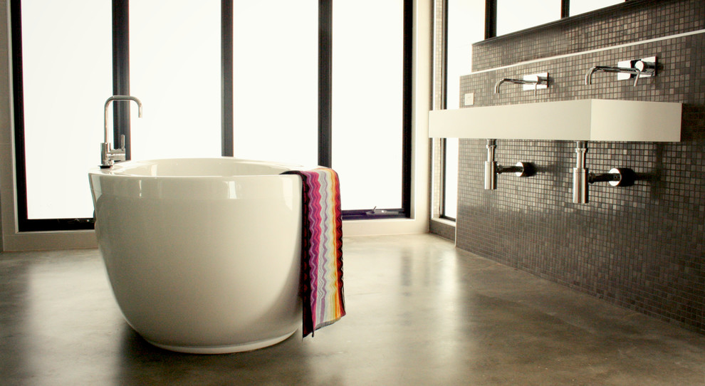 На фото: огромная главная ванная комната в современном стиле с подвесной раковиной, отдельно стоящей ванной, двойным душем, унитазом-моноблоком, столешницей из искусственного камня, серой плиткой, плиткой мозаикой, белыми стенами и бетонным полом с