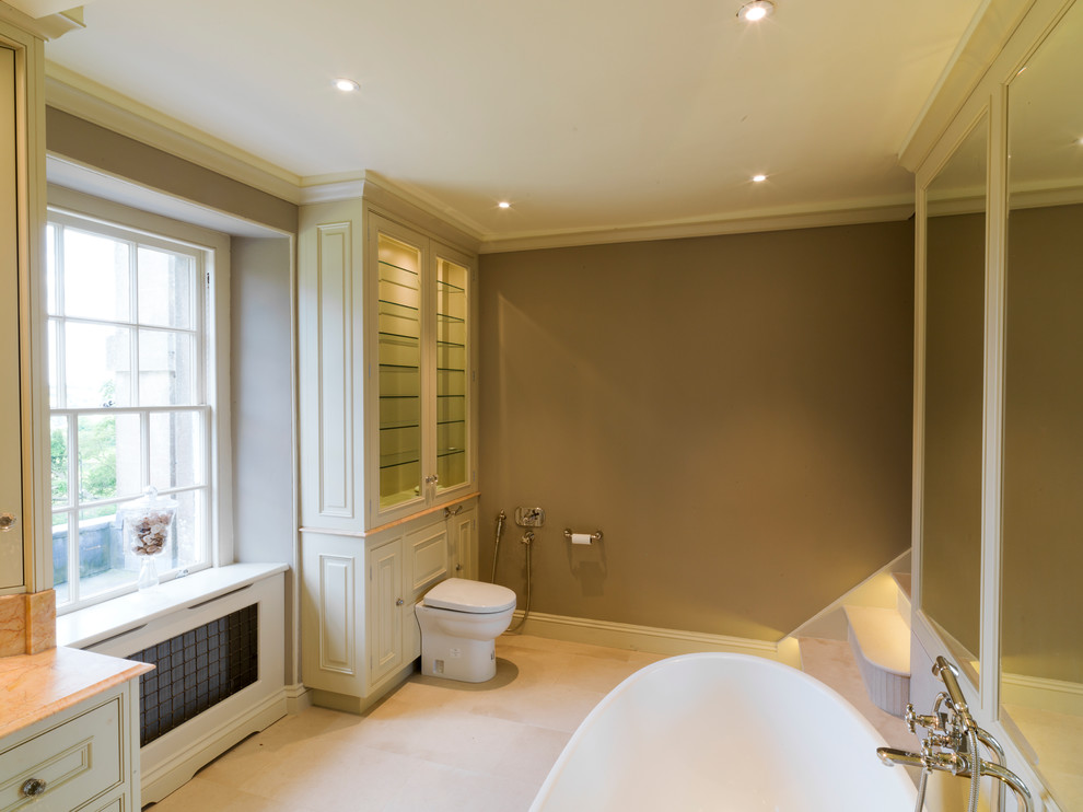 This is an example of a large ensuite bathroom in Other with a submerged sink, raised-panel cabinets, green cabinets, marble worktops, a freestanding bath, a one-piece toilet, brown walls and limestone flooring.