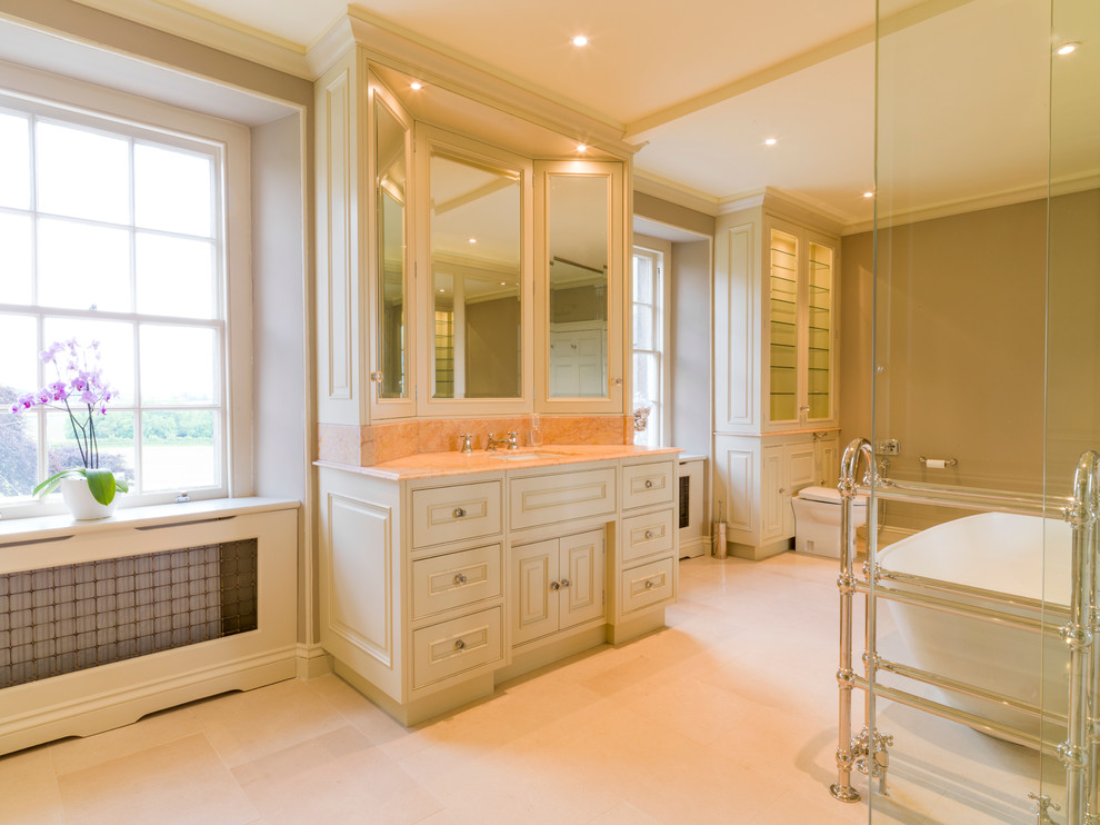Photo of a large traditional ensuite bathroom in Other with a submerged sink, raised-panel cabinets, green cabinets, marble worktops, a freestanding bath, a one-piece toilet, brown walls and limestone flooring.