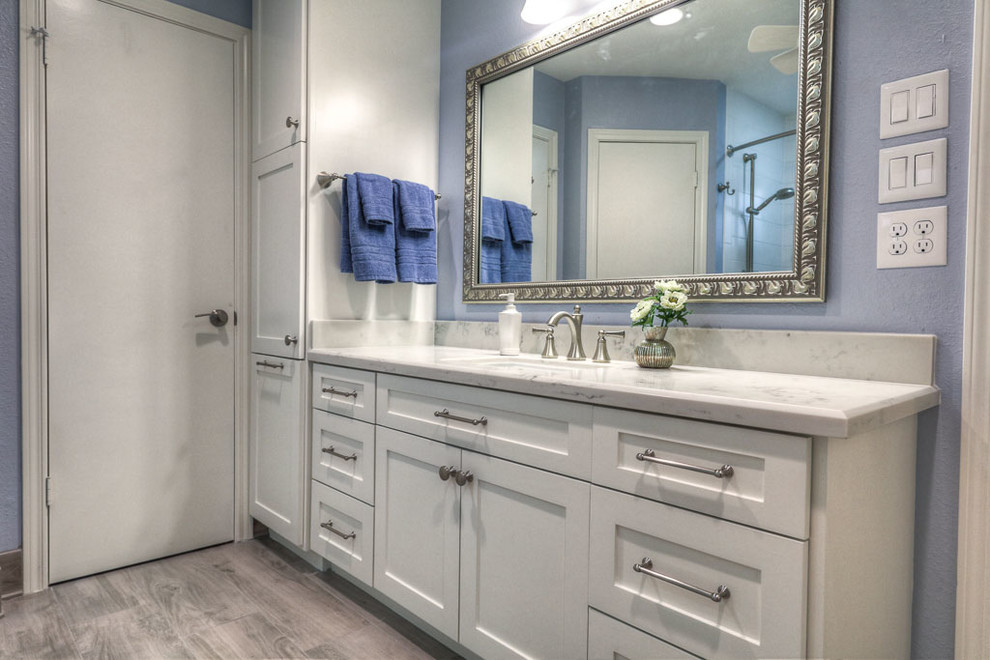 Design ideas for a large traditional ensuite bathroom in Houston with shaker cabinets, white cabinets, an alcove bath, a shower/bath combination, white tiles, porcelain tiles, blue walls, medium hardwood flooring, a submerged sink, marble worktops, brown floors and a shower curtain.
