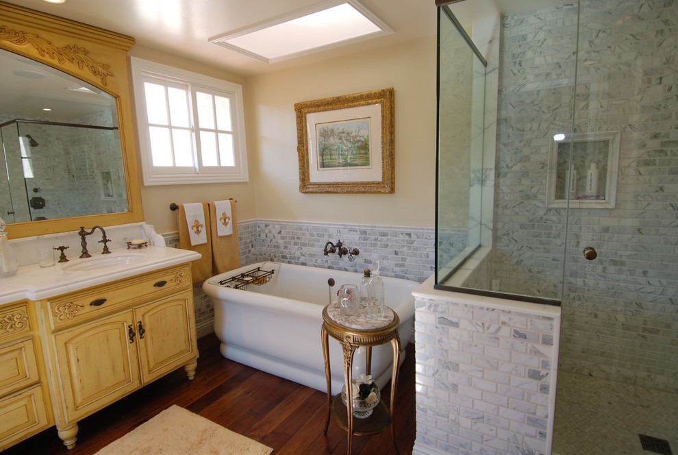 Inspiration för stora klassiska en-suite badrum, med ett undermonterad handfat, luckor med upphöjd panel, gula skåp, marmorbänkskiva, ett fristående badkar, en hörndusch, grå kakel, tunnelbanekakel, beige väggar och mellanmörkt trägolv