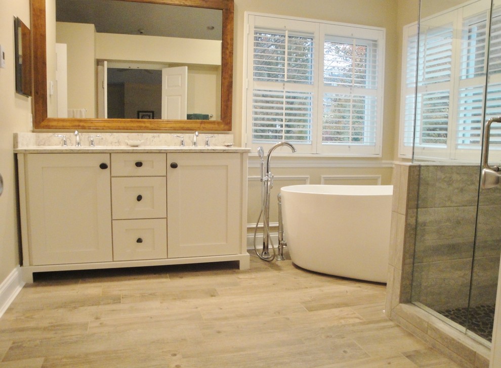 Photo of a medium sized classic ensuite bathroom in Cincinnati with recessed-panel cabinets, white cabinets, a freestanding bath, a corner shower, beige tiles, ceramic tiles, beige walls, light hardwood flooring, a submerged sink, beige floors and a hinged door.