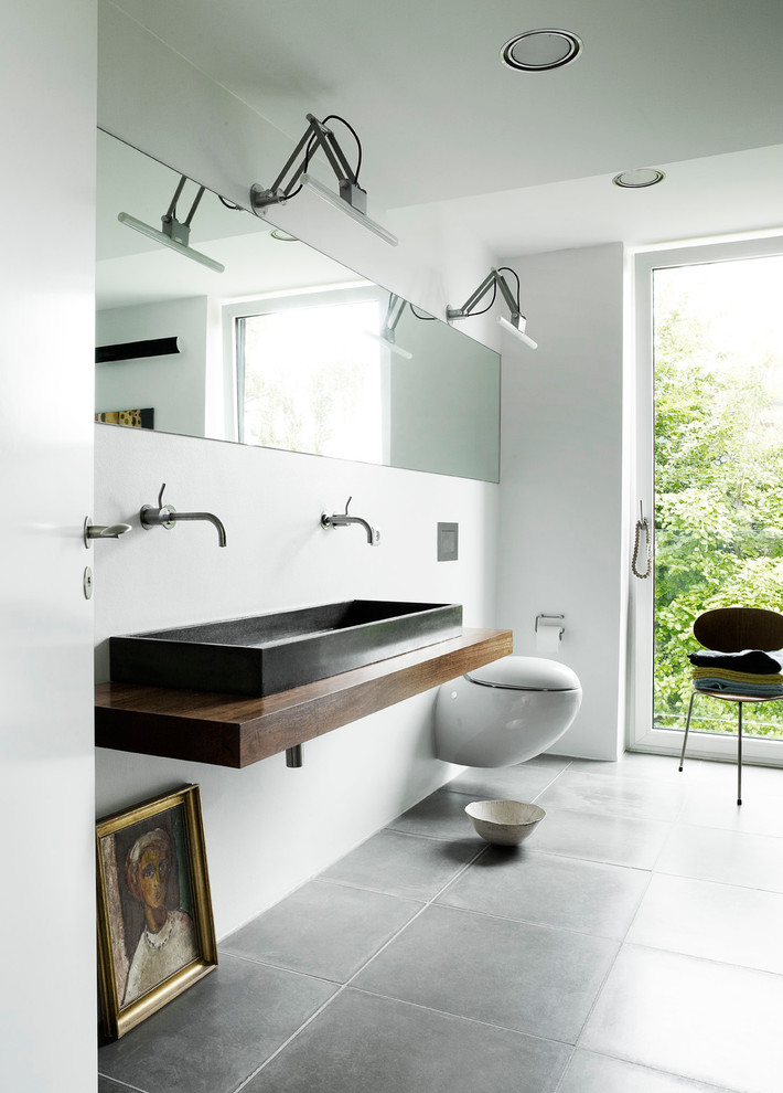 Modelo de cuarto de baño actual de tamaño medio con sanitario de pared, paredes blancas, suelo de pizarra, encimera de madera y suelo gris