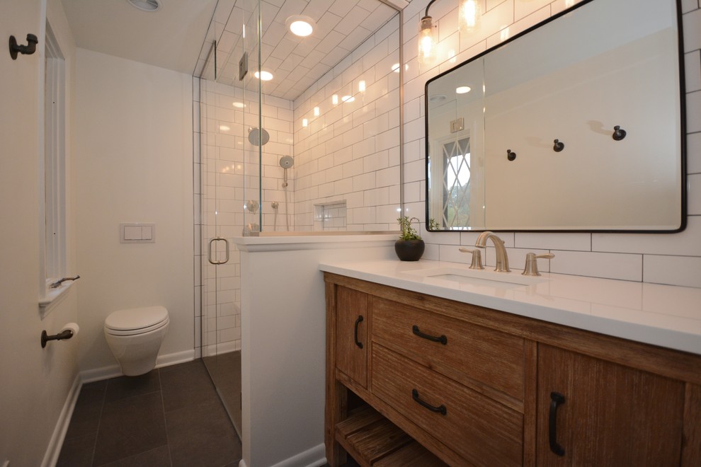 Medium sized classic bathroom in Other with flat-panel cabinets, medium wood cabinets, a corner shower, a wall mounted toilet, white tiles, metro tiles, white walls, cement flooring, a submerged sink, engineered stone worktops, grey floors, a hinged door and white worktops.