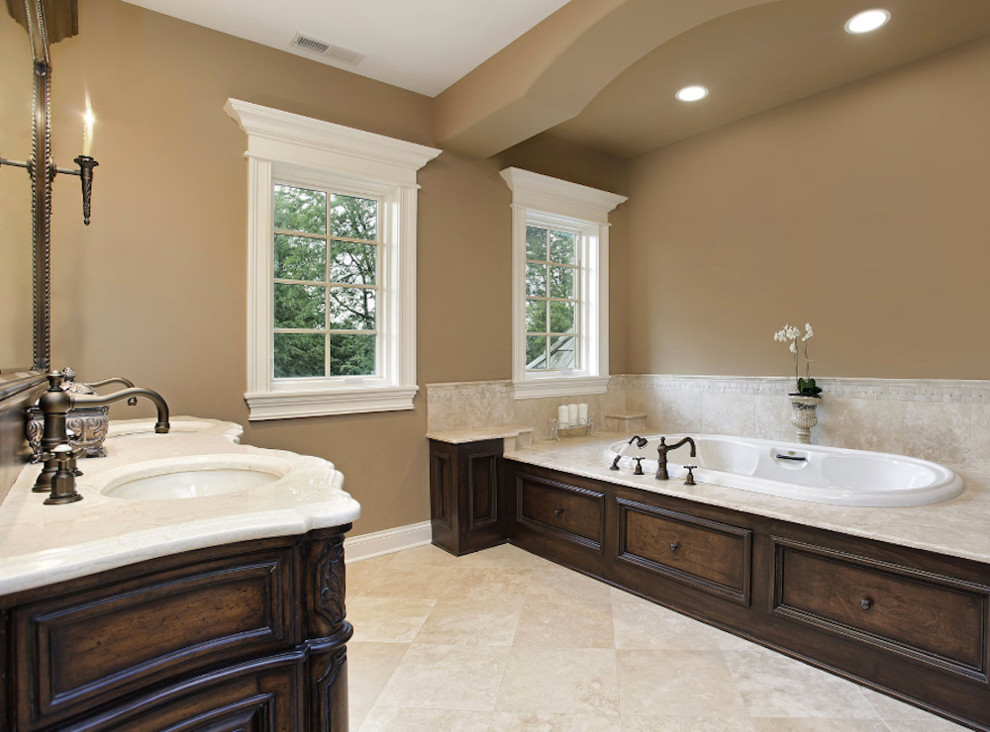 Inspiration for a mid-sized timeless 3/4 beige tile and porcelain tile travertine floor and beige floor bathroom remodel in Phoenix with an integrated sink, recessed-panel cabinets, dark wood cabinets, marble countertops, an undermount tub and brown walls