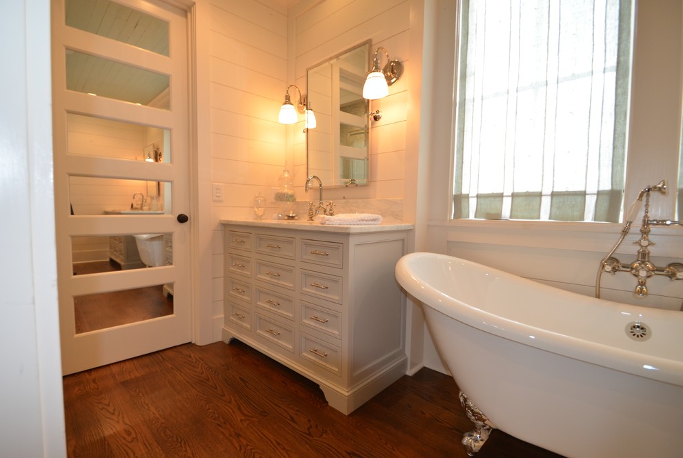 Bild på ett mellanstort vintage en-suite badrum, med luckor med upphöjd panel, grå skåp, ett badkar med tassar, vita väggar, mellanmörkt trägolv, ett undermonterad handfat och marmorbänkskiva
