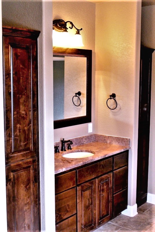 Пример оригинального дизайна: ванная комната в классическом стиле с фасадами с выступающей филенкой, фасадами цвета дерева среднего тона, столешницей из гранита, бежевыми стенами, полом из керамогранита, врезной раковиной, бежевым полом и разноцветной столешницей