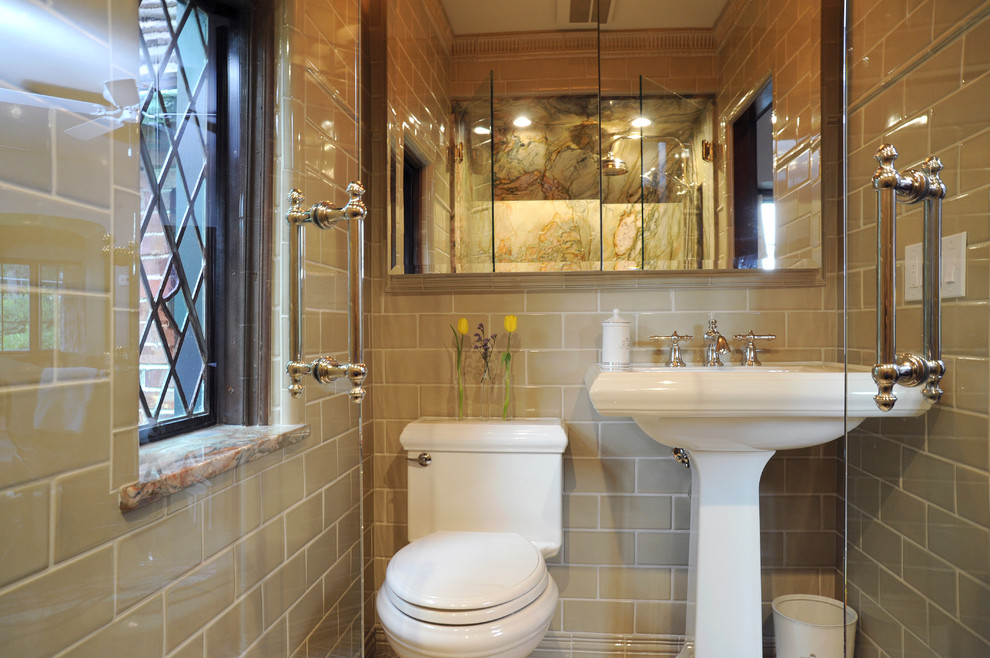 Klassisk inredning av ett litet en-suite badrum, med ett piedestal handfat, en dusch i en alkov, en toalettstol med separat cisternkåpa, beige kakel, keramikplattor, beige väggar och klinkergolv i keramik