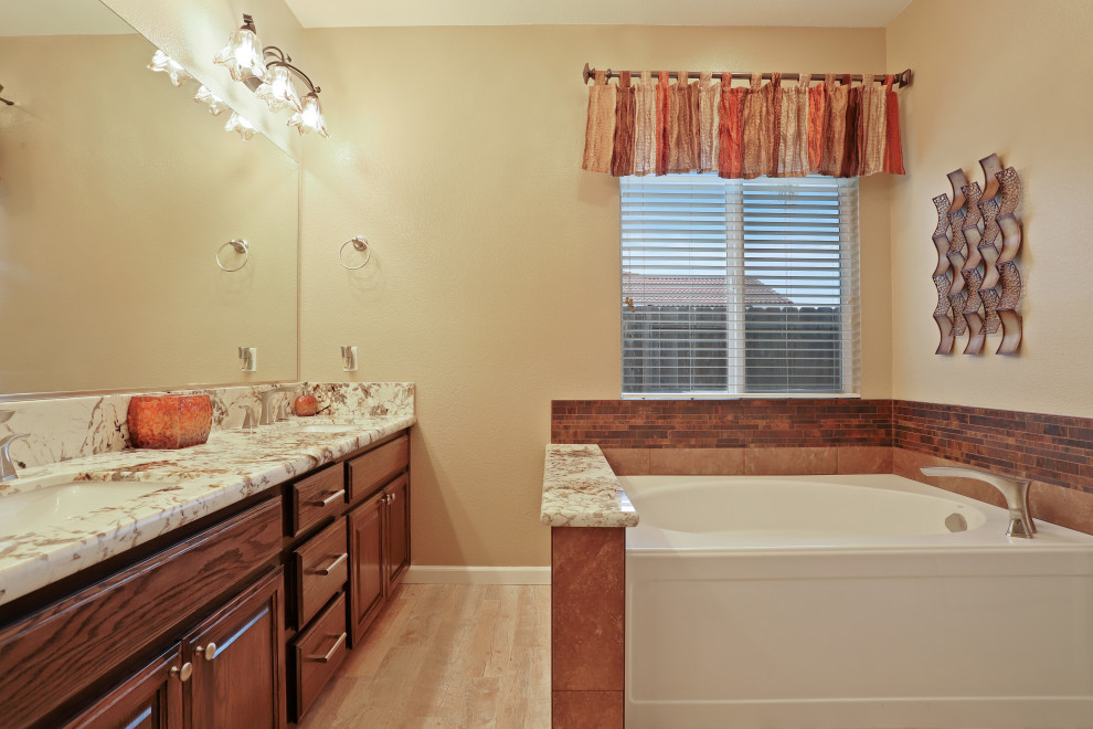 Klassisk inredning av ett beige beige badrum, med skåp i mellenmörkt trä, en hörndusch, en vägghängd toalettstol, beige kakel, beige väggar, klinkergolv i porslin, ett undermonterad handfat, granitbänkskiva, brunt golv och dusch med gångjärnsdörr