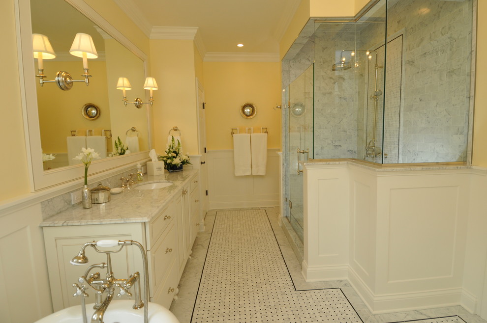 Klassisk inredning av ett mellanstort badrum, med ett undermonterad handfat, möbel-liknande, vita skåp, marmorbänkskiva, ett badkar med tassar, vit kakel, stenkakel, gula väggar och marmorgolv