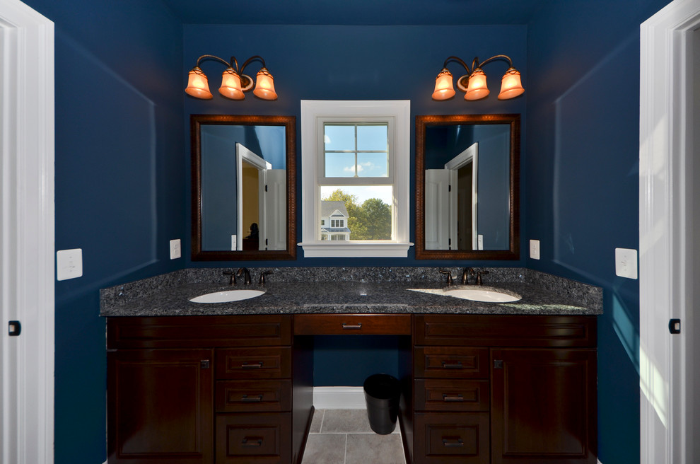 Cette image montre une grande salle de bain design en bois foncé avec un placard avec porte à panneau surélevé, un mur bleu, un sol en ardoise, un lavabo encastré et un plan de toilette en granite.