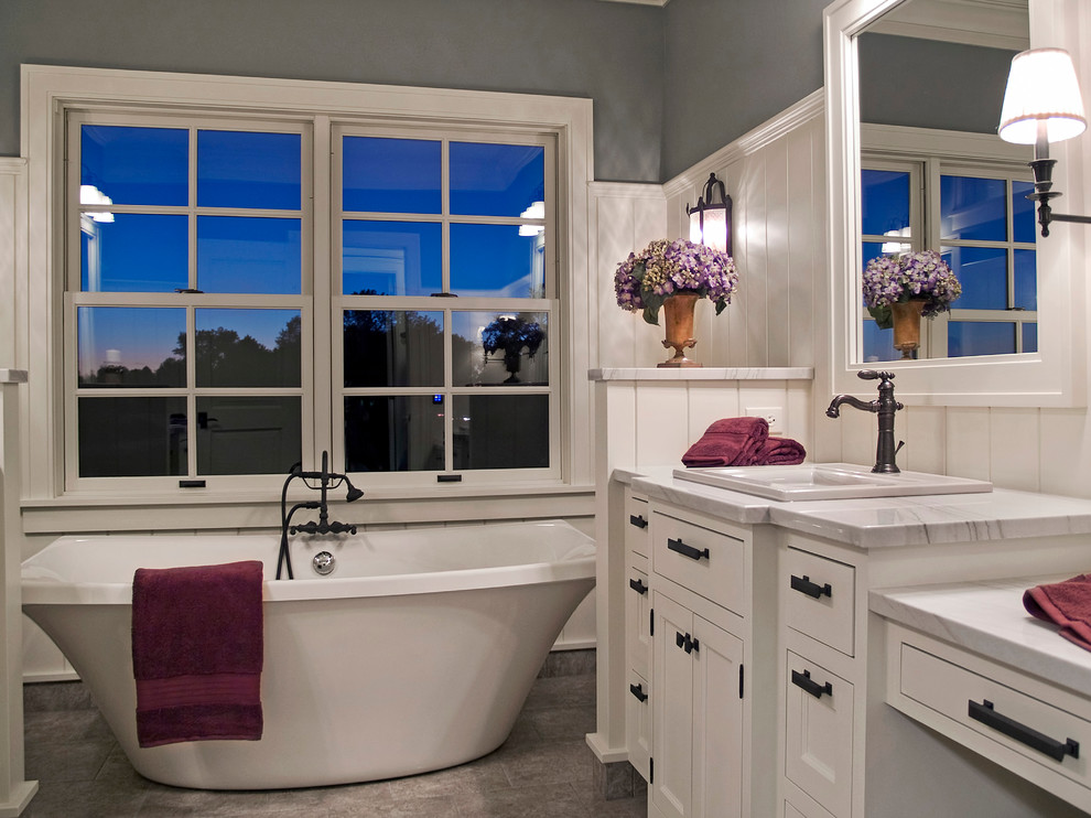 Aménagement d'une salle de bain classique avec un lavabo posé, un placard avec porte à panneau encastré, des portes de placard blanches, une baignoire indépendante et un mur gris.