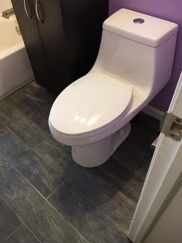 Small modern shower room bathroom in Baltimore with flat-panel cabinets, black cabinets, a shower/bath combination, purple walls, a corner bath, a one-piece toilet, painted wood flooring, a built-in sink and solid surface worktops.
