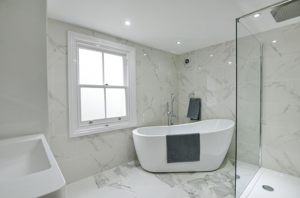 Photo of a large modern family bathroom in London with flat-panel cabinets, white cabinets, a freestanding bath, a walk-in shower, a wall mounted toilet, white tiles, porcelain tiles, white walls, a wall-mounted sink and solid surface worktops.