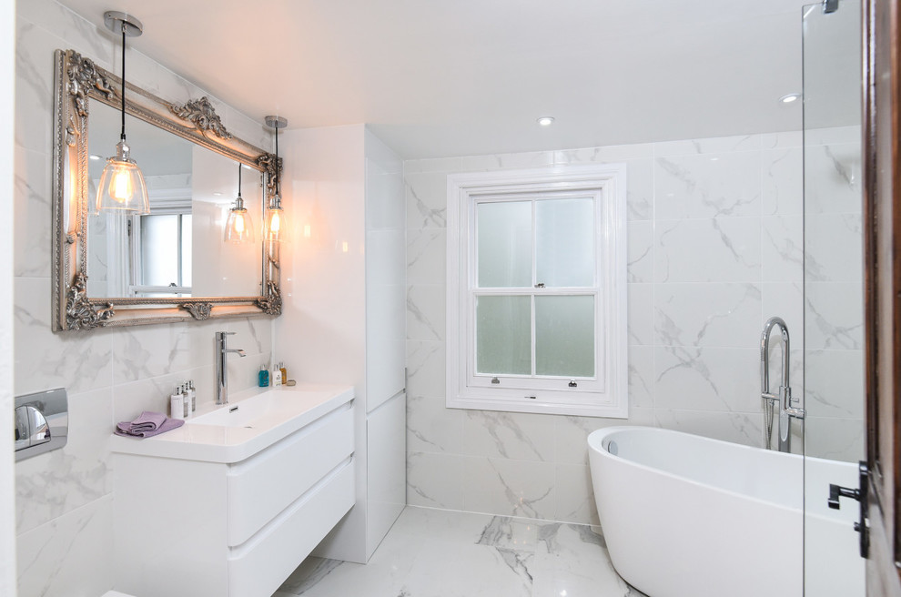 Large modern family bathroom in London with flat-panel cabinets, white cabinets, a freestanding bath, a walk-in shower, a wall mounted toilet, white tiles, porcelain tiles, white walls, a wall-mounted sink and solid surface worktops.
