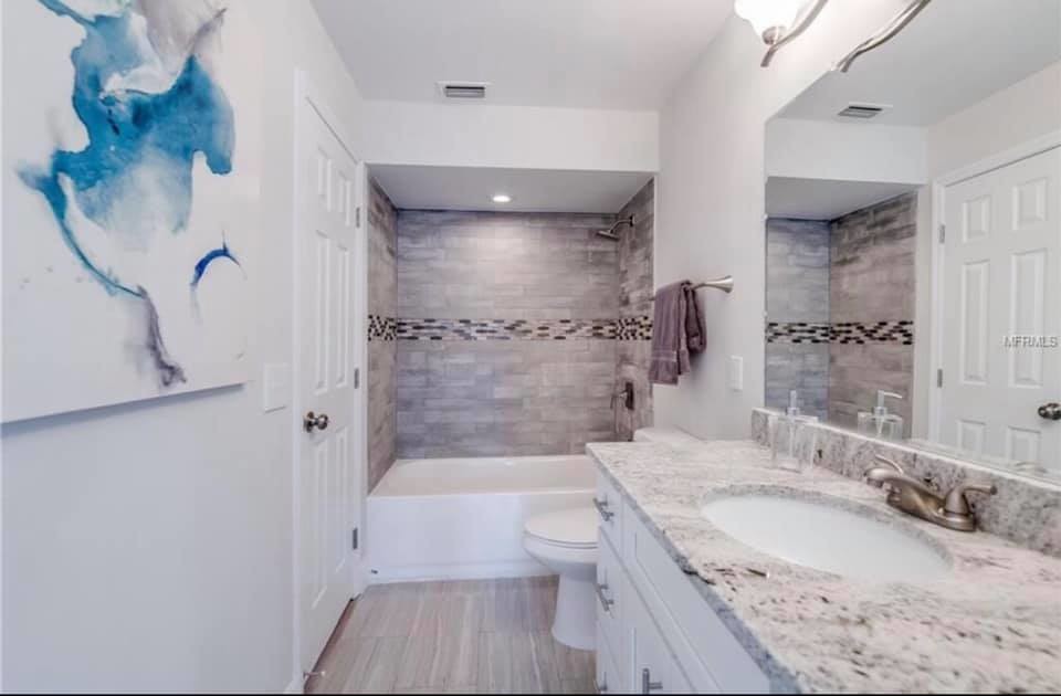 На фото: ванная комната в стиле неоклассика (современная классика) с фасадами в стиле шейкер, белыми фасадами, ванной в нише, белыми стенами, врезной раковиной, столешницей из гранита, разноцветным полом и разноцветной столешницей