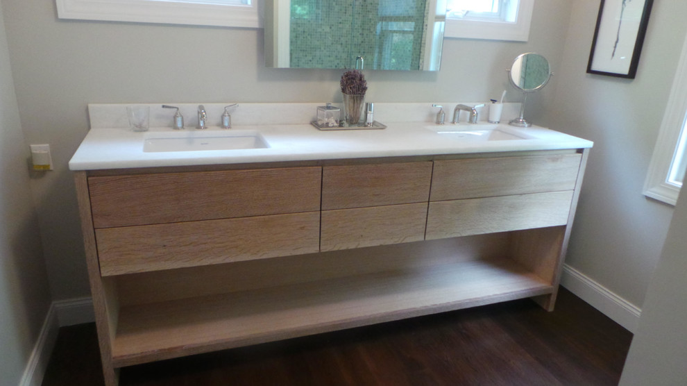 Kleines Modernes Badezimmer En Suite mit flächenbündigen Schrankfronten, hellen Holzschränken, grauer Wandfarbe, dunklem Holzboden, Unterbauwaschbecken, Duschnische, Mineralwerkstoff-Waschtisch, braunem Boden und Falttür-Duschabtrennung in New York