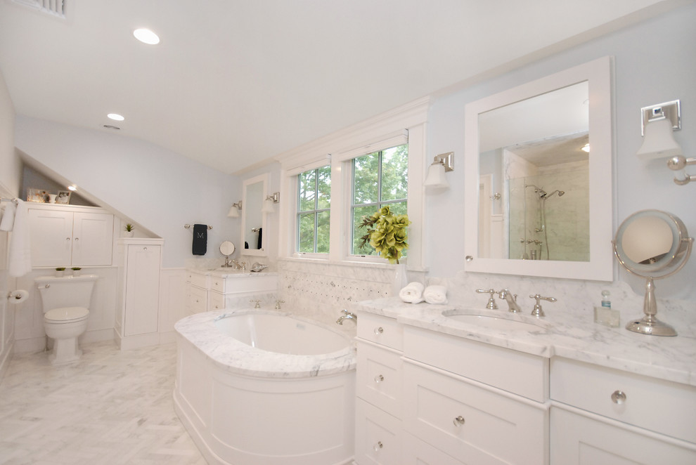 This is an example of a large ensuite bathroom in New York with shaker cabinets, white cabinets, a submerged bath, a one-piece toilet, white tiles, white walls, marble flooring and a submerged sink.