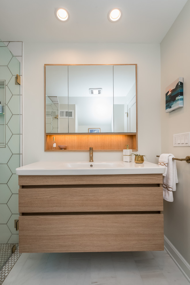 Walk-in shower - small transitional master white tile and ceramic tile marble floor and white floor walk-in shower idea in New York with flat-panel cabinets, light wood cabinets, a wall-mount toilet, white walls, an integrated sink, solid surface countertops, a hinged shower door and white countertops