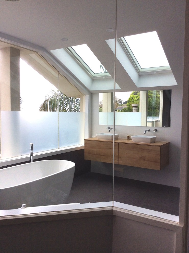 Ejemplo de cuarto de baño moderno con lavabo sobreencimera, bañera exenta, ducha abierta, sanitario de pared, paredes blancas y suelo de baldosas de porcelana
