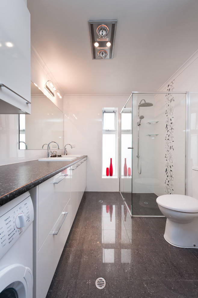 Photo of a small modern shower room bathroom in Other with a built-in sink, white cabinets, an alcove shower, a one-piece toilet, white tiles, white walls and a laundry area.